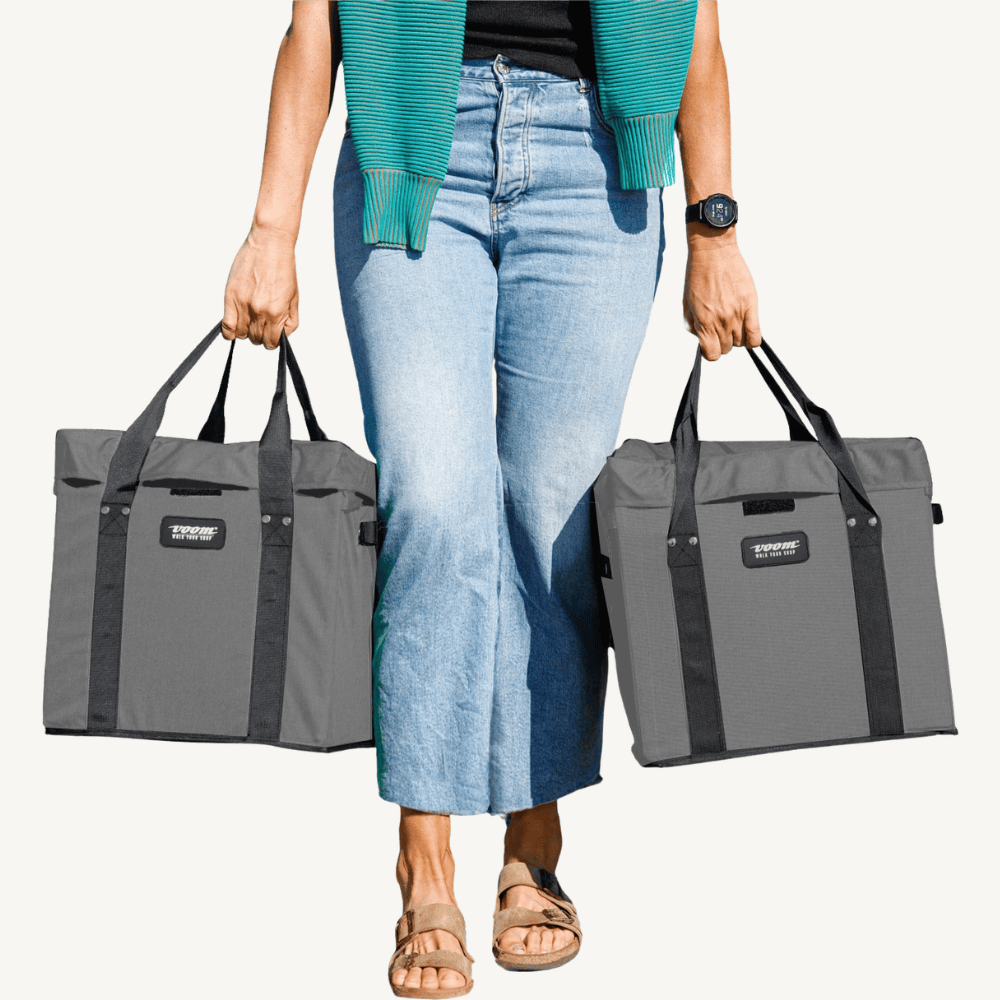 Person holding two gray VOOMcart easy to carry grocery bins with black handles on a white background